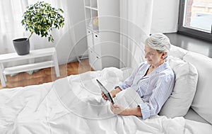 senior woman with tablet pc in bed at home bedroom