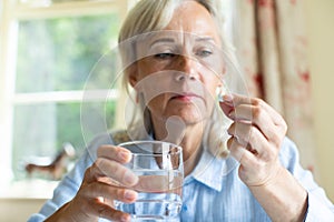 Senior Woman Taking Tablet With Glass Of Water At Home photo