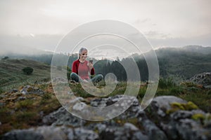 Senior woman taking selfie when doing breathing exercise in nature on early morning with fog and mountains in background