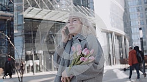 A senior woman talking by phone holding tulips outdoors