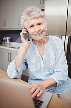 Senior woman talking on phone and using laptop