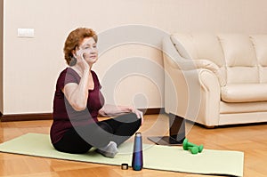 Senior woman talking on the smartphone during fitness sports exercising at home online with personal trainer.