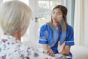 Senior woman talking to young care nurse on home visit