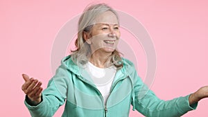 Senior woman in teal hoodie expresses gratitude, pink background