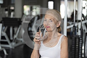 Senior woman thirsty drinking water after exercise in fitness gym. elderly healthy lifestyle