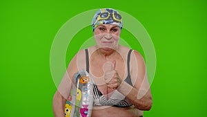 Senior woman tourist in swimsuit bra, swim goggles with swimming ring asking to follow, join