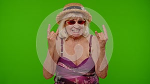Senior woman tourist in swimsuit dancing, celebrating, showing tongue, rock and roll hand gesture