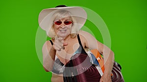 Senior woman tourist in swimsuit with luggage, passport, tickets asking to follow join on chroma key