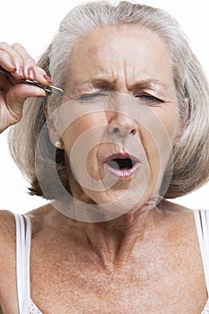 Senior woman tweezing eyebrows against white background
