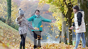 Senior woman and two young girls her granddaughters throwing fallen autumn leaves up in the air, while on a walk outside