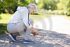 Senior woman tying sport shoe laces at summer park