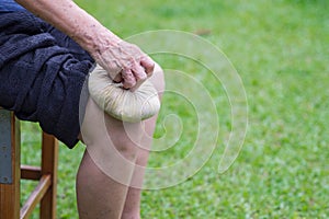 A senior woman uses a Thai herbal compress ball on the knee. Knee pain may cause by muscle strain, tendinosis, osteoarthritis OA