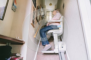 Senior woman using automatic stair lift on a staircase at her home. Medical Stairlift for disabled people and elderly