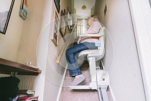 Senior woman using automatic stair lift on a staircase at her home. Medical Stairlift for disabled people and elderly photo