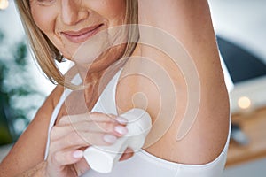 Senior woman using deo roll-on in the bathroom