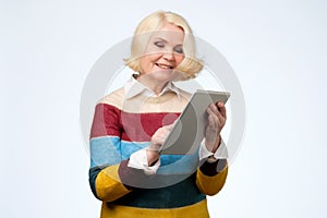 Senior woman using digital tablet surfing web media chatting online, smiling.