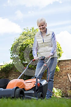 Senior Woman Using Electric Lawn Mower To Cut Grass At Home