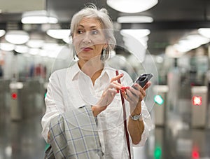 Senior woman using her phone at entrance to subway station