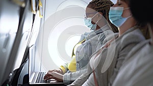 Senior woman using laptop during airplane trip while wearing facemask