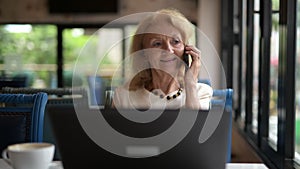 Senior woman using laptop computer and talking on mobile phone