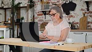 Senior Woman Using Laptop in the Kitchen at Home