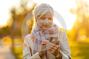 Senior woman using mobile phone outdoors in autumn