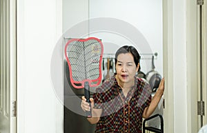 Senior woman using mosquito swatter at home,Female with mosquito electric net racket in bedroom