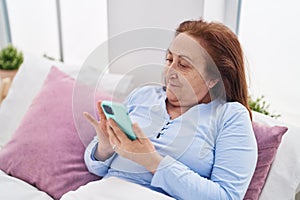 Senior woman using smartphone sitting on bed at bedroom