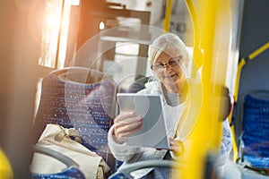 Senior woman using tablet, while riding public bus