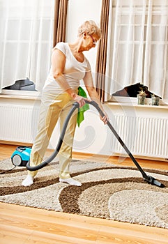 Senior woman vacuuming carpet at home