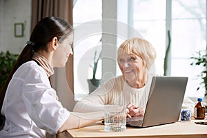 Senior woman visiting doctor, sitting at table in office, having appointment and consultation. Women smiling and talking