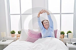 Senior woman waking up stretching arms at bedroom
