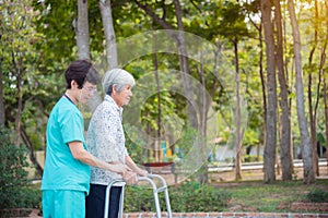 Senior woman walking with assistance from nurse in hospital park