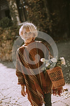 Senior woman walking with basket full of flowers and groceries in autumn park