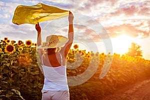 Senior woman walking in blooming sunflower field raising hands with scarf and having fun. Summer vacation