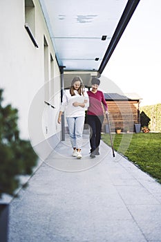 Senior woman walking with her nurse by the side of the house to the garden on a sunny day