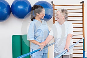 Senior woman walking with parallel bars with therapist