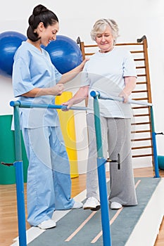 Senior woman walking with parallel bars with therapist