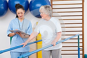 Senior woman walking with parallel bars with therapist