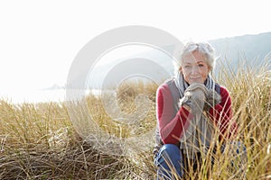 Senior Woman Walking Through Sand Dunes On Winter Beach