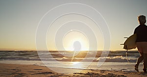 Senior woman walking with surfboard at the beach