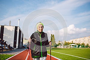 Senior woman walking with walking poles in stadium on a red rubber cover. Elderly woman 88 years old doing Nordic walking