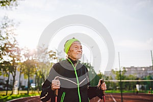 Senior woman walking with walking poles in stadium on a red rubber cover. Elderly woman 88 years old doing Nordic walking