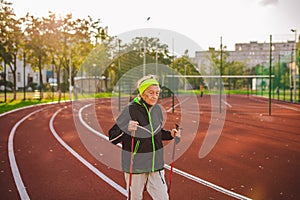 Senior woman walking with walking poles in stadium on a red rubber cover. Elderly woman 88 years old doing Nordic walking