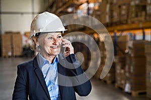 Senior woman warehouse manager or supervisor with smartphone.