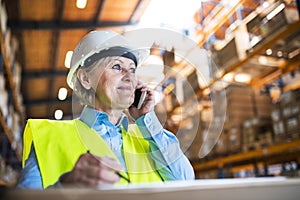 Senior woman warehouse manager or supervisor with smartphone, making phone call.