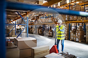 A senior woman warehouse worker pulling a pallet truck with boxes.