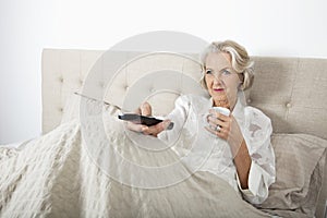 Senior woman watching TV while having coffee in bed