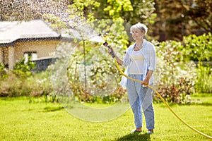 Senior woman watering lawn by hose at garden