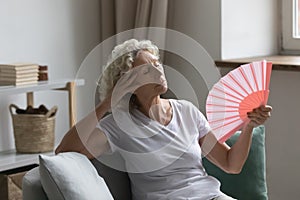 Senior woman waving fan feels unwell due unbearable hot weather